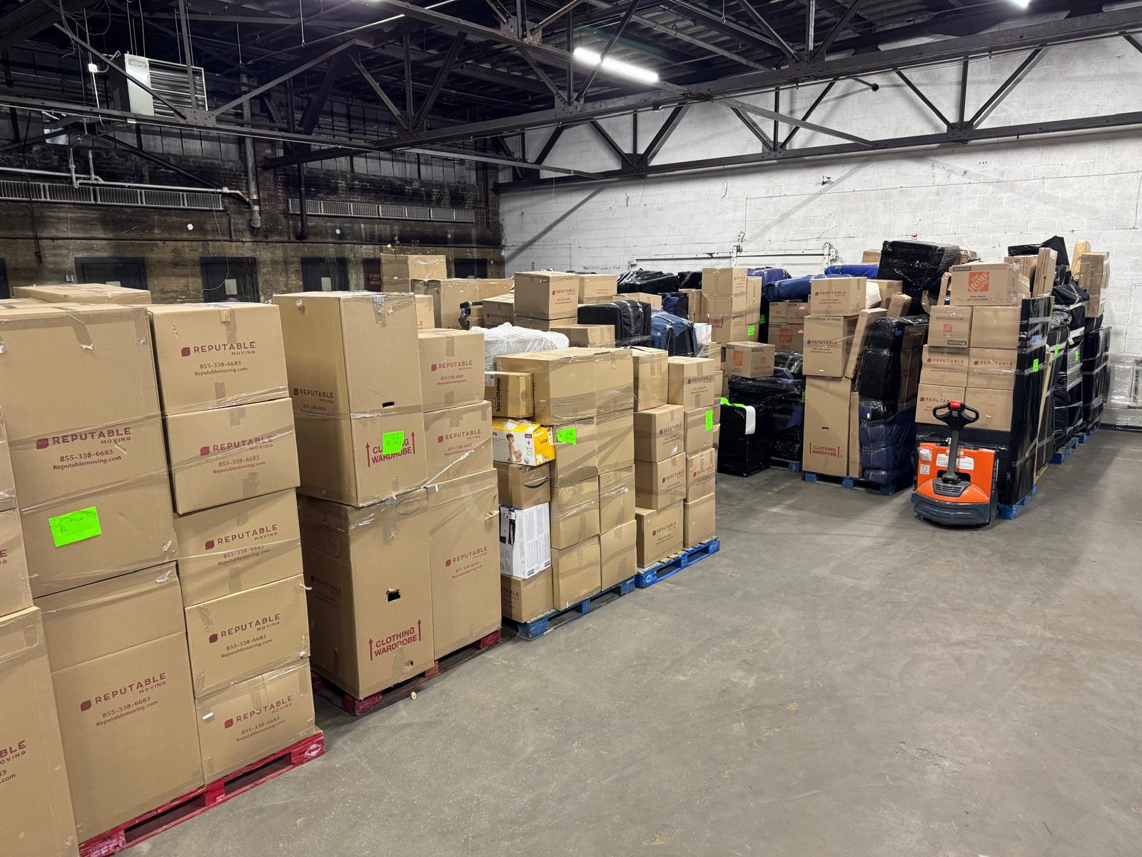 Reputable warehouse interior with pallets of branded boxes on industrial racks and an electric pallet jack