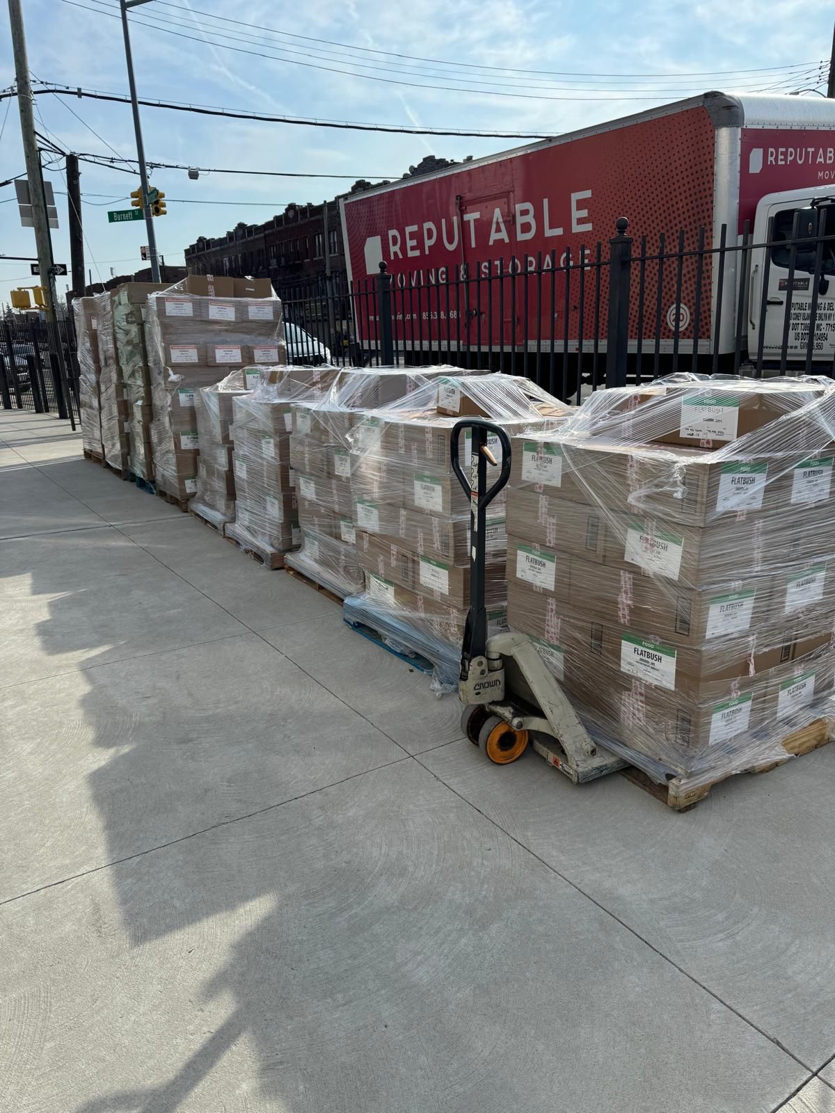 Outdoor warehouse staging area with rows of shrink-wrapped pallets and a Reputable truck